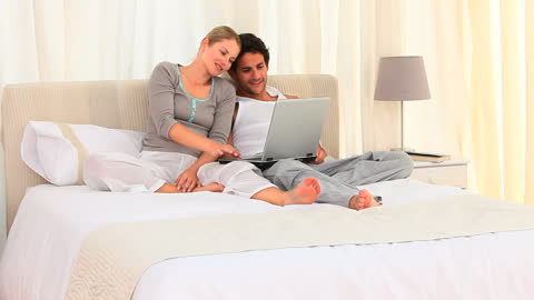 Happy Couple Relaxing in Bed with Laptop at Home