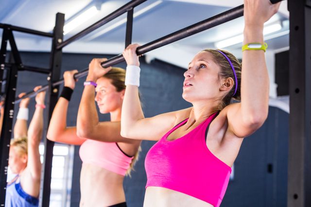 Women are performing chin-ups in a gym, showcasing strength and determination. Ideal for use in fitness blogs, workout programs, gym advertisements, and health and wellness articles.
