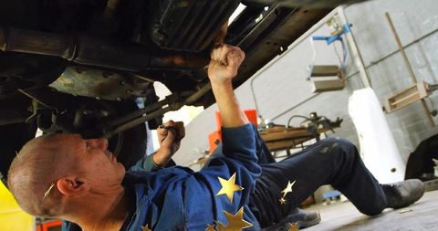 Mechanic Tightening Suspension Under Vehicle in Garage