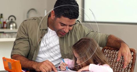 Father guiding daughter writing at kitchen table during homework and bonding time