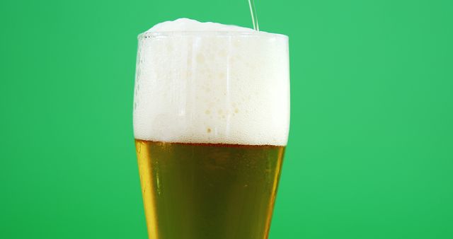 This close-up image depicts a refreshing beer being poured into a glass with a foamy head, set against a vibrant green background. Ideal for use in advertisements for breweries, pubs, and bars, as well as promotional material for beer festivals and beverage menus.