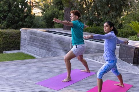 Friends practicing yoga outdoors on wooden deck in warrior ii pose