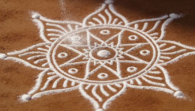 White kolam rangoli mandala featuring falling powder on earthen clay floor
