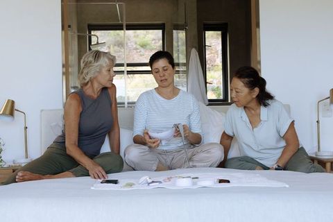 Three women exploring handheld wellness device on bed, casual tech discussion at home