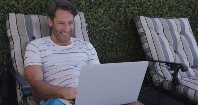 Smiling Man Using Laptop While Relaxing on Patio Loungers - Download Free Stock Images Pikwizard.com