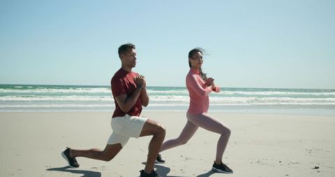 Midadult diverse couple performing lunges on sunny shoreline outdoor fitness wellness