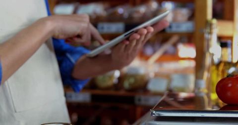 Aproned Worker Using Tablet in Grocery Store with Fresh Products