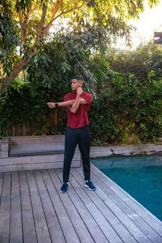 Man Stretching on Wooden Deck Near Swimming Pool in Serene Backyard