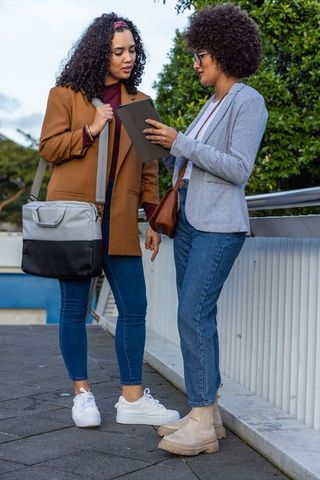 Diverse female colleagues collaborating on tablet on urban walkway by metal railing