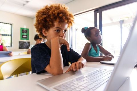 Curious elementary children focusing on laptops and tablets in bright classroom