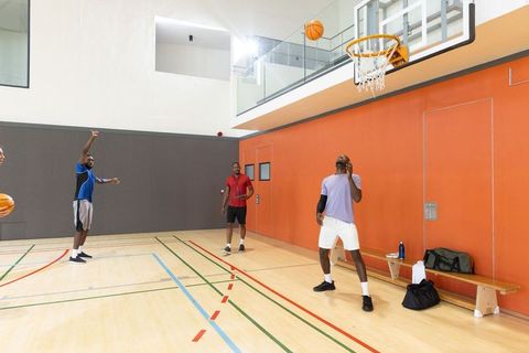 Diverse men practicing basketball on indoor court under hoop and bench for team training