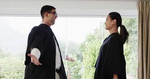 Joyful asian couple in graduation gowns celebrating together