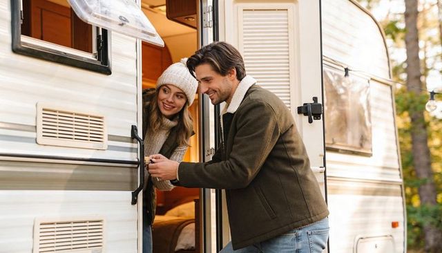 Couple securing caravan door at autumn campsite smiling outdoors