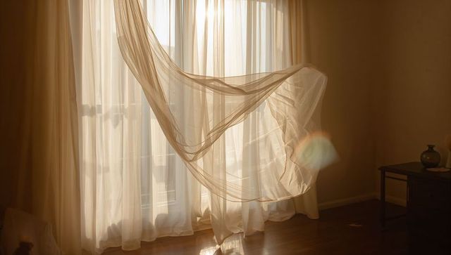 Sunlit sheer curtain billowing over hardwood floor with soft amber glow and lens flare