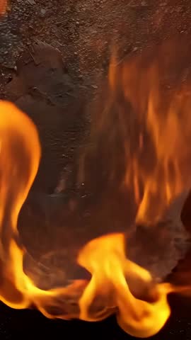 Vertical video showing sparking orange flames burning charred sheets on asphalt with glowing embers