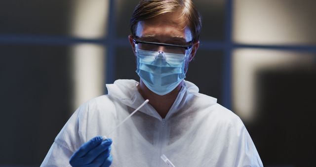 A male scientist in a protective suit, face mask, and glasses is handling a sample with swabs. This image is ideal for use in contexts such as science research, healthcare, medical studies, safety protocols, clinical testing, and infection control. It emphasizes the importance of safety measures and accuracy in scientific work, particularly in the medical and research fields.