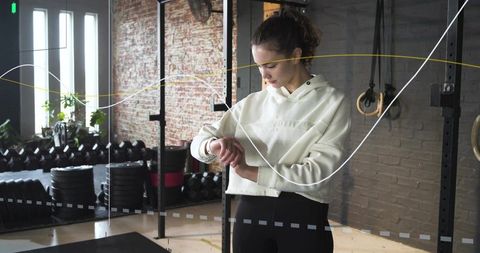 Young woman checking smartwatch and tracking workout metrics in gym with data overlays