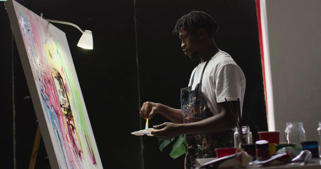 African american male artist wearing apron painting on canvas at art studio. art, hobby and creative occupation concept