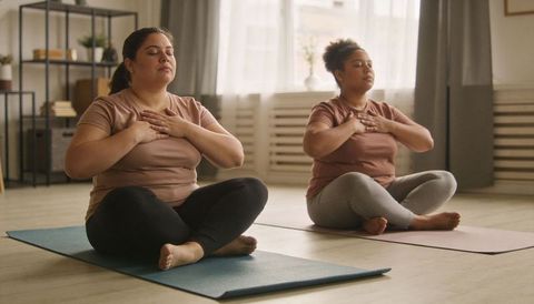 Plus-Size Women Practicing Mindful Breathing on Yoga Mats in Sunlit Home Studio