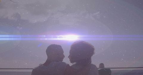 Silhouetted couple leaning together on waterfront pier with dramatic lens flare