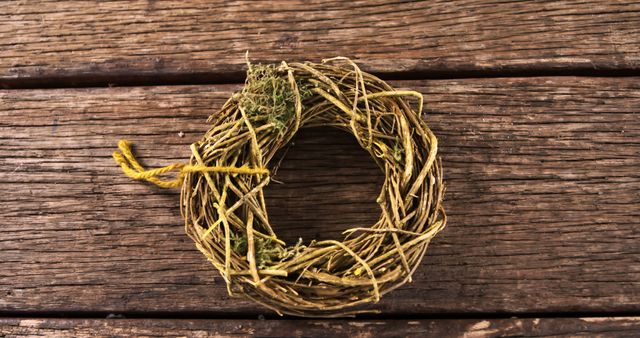A rustic wreath made of twigs and dried plants rests on a wooden surface, symbolizing seasonal decor or a natural craft project. Its simplicity and handmade charm evoke a sense of countryside aesthetics or eco-friendly decoration.