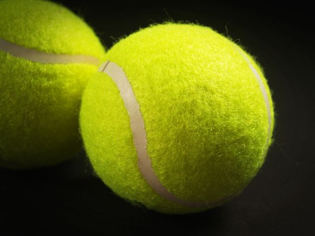Close-up of two bright yellow tennis balls with sharp focus enhances the texture and details, suitable for sporting event promotions, tennis gear advertisements, blog illustrations, and educational materials about tennis.