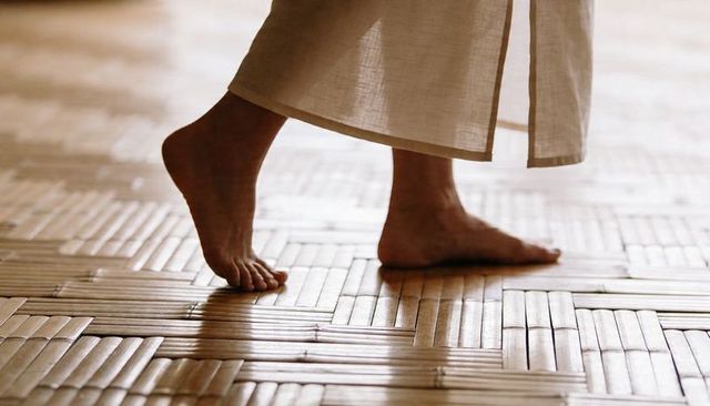 Walking barefoot on woven parquet floor wearing flowing linen skirt low-angle closeup