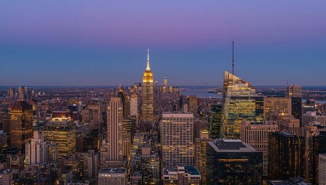 Twilight manhattan skyline featuring illuminated empire state crown and slanted glass tower