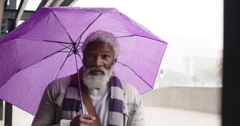 Senior African American Man Holding Purple Umbrella on Rainy Urban Walkway During Commute