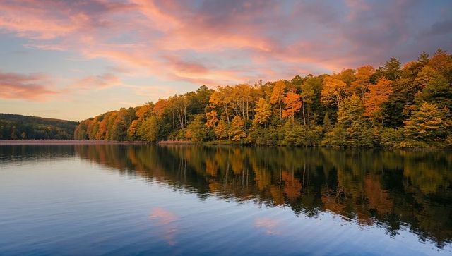 Sunset over autumn lake reflecting colorful treeline and pink cloud reflections