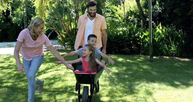 Happy Family Playing Outdoors with Wheelbarrow in Sunlit Garden - Download Free Stock Images Pikwizard.com