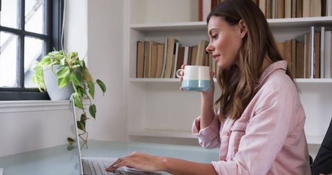Woman Enjoying Coffee While Using Laptop in Bright Office