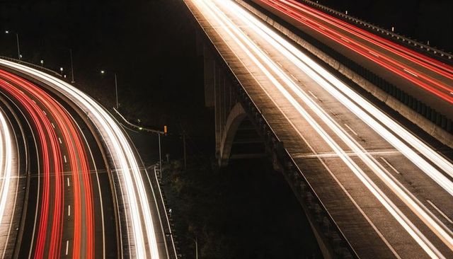 Streaming light trails curving across multi-lane highway and overpass at night