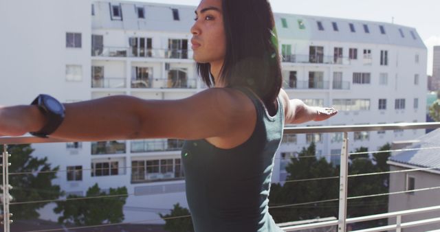 Young woman practicing yoga on an urban balcony, showing a calm and focused expression. Perfect for content related to fitness, yoga instruction, mindfulness, outdoor activities, health, well-being, and urban lifestyle.