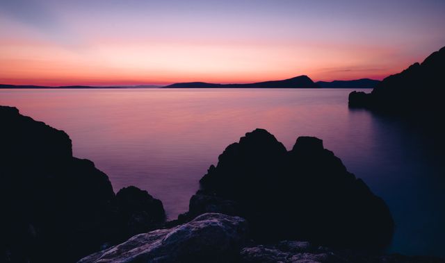 Beautiful twilight scene at rocky coastline with calm sea and serene colors in the sky, perfect for backgrounds, screensavers, travel websites, relaxation themes, and nature-related articles.