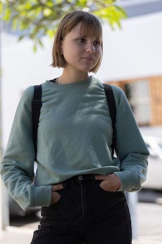 Young woman standing on urban sidewalk wearing sage-green sweatshirt and high-waisted jeans