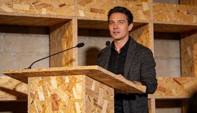 Confident male presenter speaking at oriented strand board lectern in industrial workshop