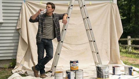 Man taking water break during exterior painting project leaning on ladder with paint cans