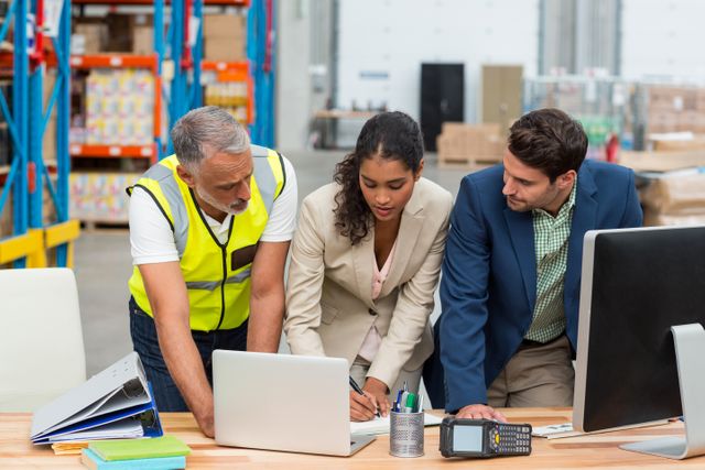 Diverse team of professionals collaborating in a warehouse office. Ideal for illustrating teamwork, logistics planning, and business operations in an industrial setting. Useful for articles, presentations, and websites related to warehouse management, logistics, and business collaboration.
