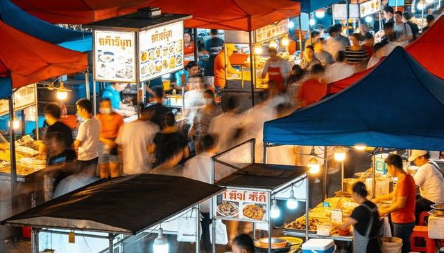 Vibrant thai night market with grilling vendors serving street food under colorful tents