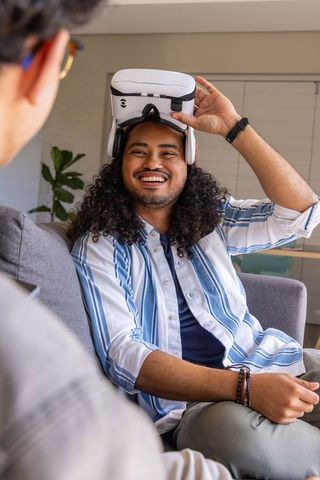 Friends trying virtual reality headset on sofa, laughing and interacting in modern home