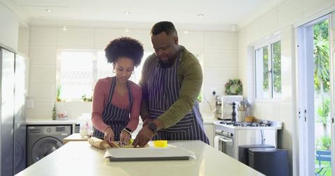 Mid-adult couple baking cookies at bright modern kitchen island, kneading dough together