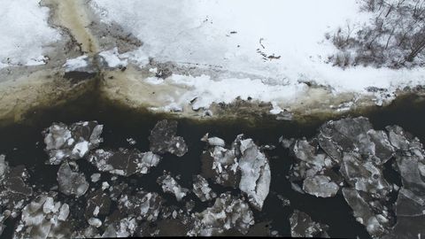 Aerial winter river with melting ice floes and snow-covered bank