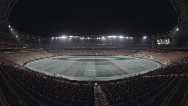 Empty oval stadium glowing under floodlights at night, panoramic sports arena interior