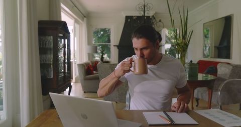 Man Sipping Coffee While Planning on Laptop at Home