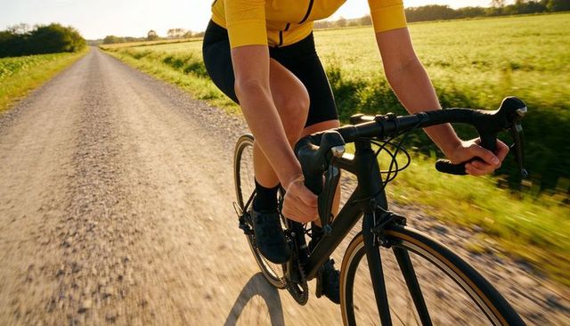Gravel road cycling close-up: pedaling rider in yellow jersey gripping brake hoods at speed