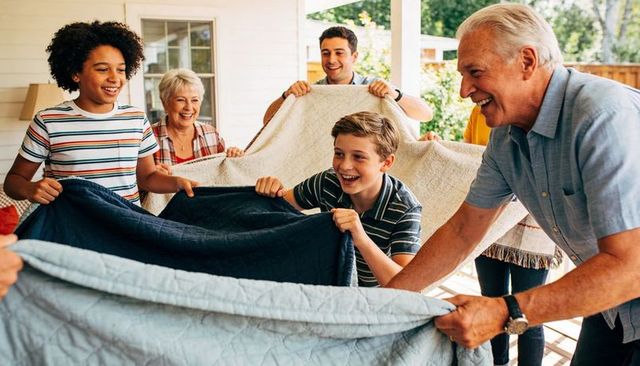 Multigenerational family laughing and playing with quilts on sunny porch, bonding moments