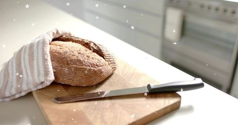 Sunlit rustic artisan wholegrain loaf on wooden board with striped towel and serrated knife