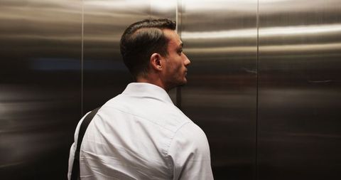 Professional man standing alone in elevator holding bag