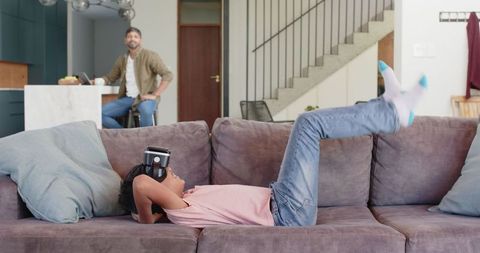 Boy Enjoying Virtual Reality on Sofa, Parent Observing From Kitchen Area